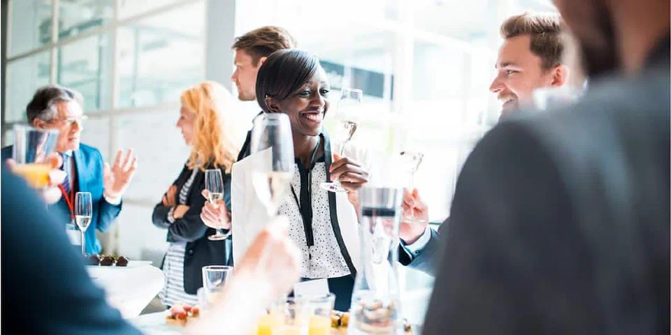 A group of people standing around a table drinking sparkling wine.
