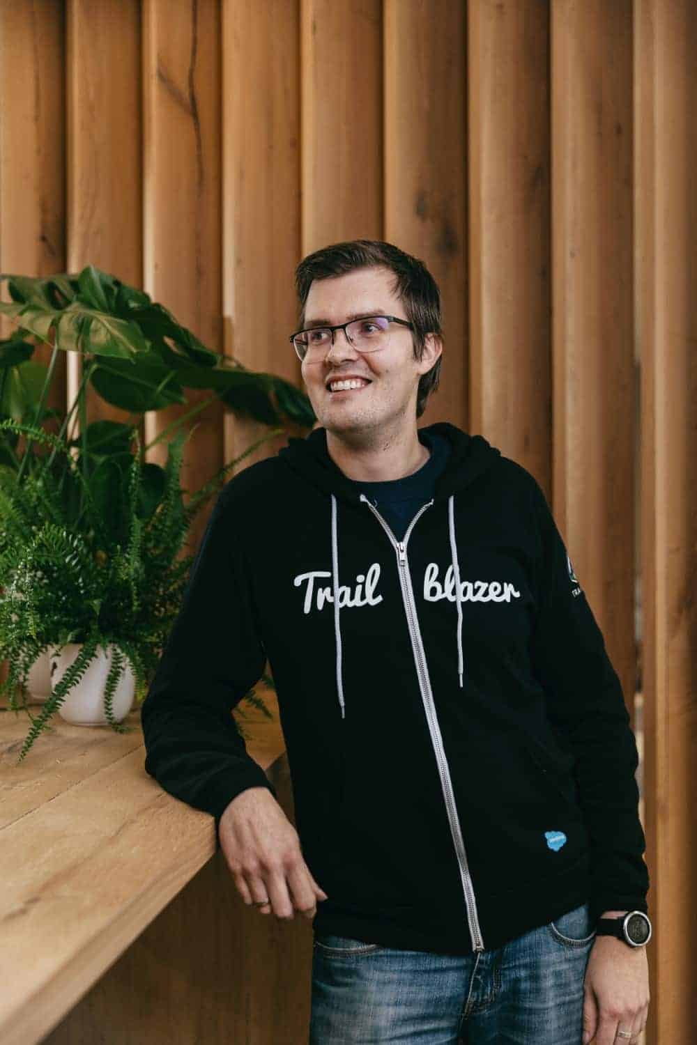 A picture of Thomas Theunen leaning on a desk at the office with plants on the background.