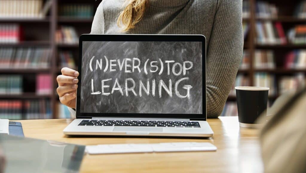 A women holding a laptop displaying the text “never stop learning”.