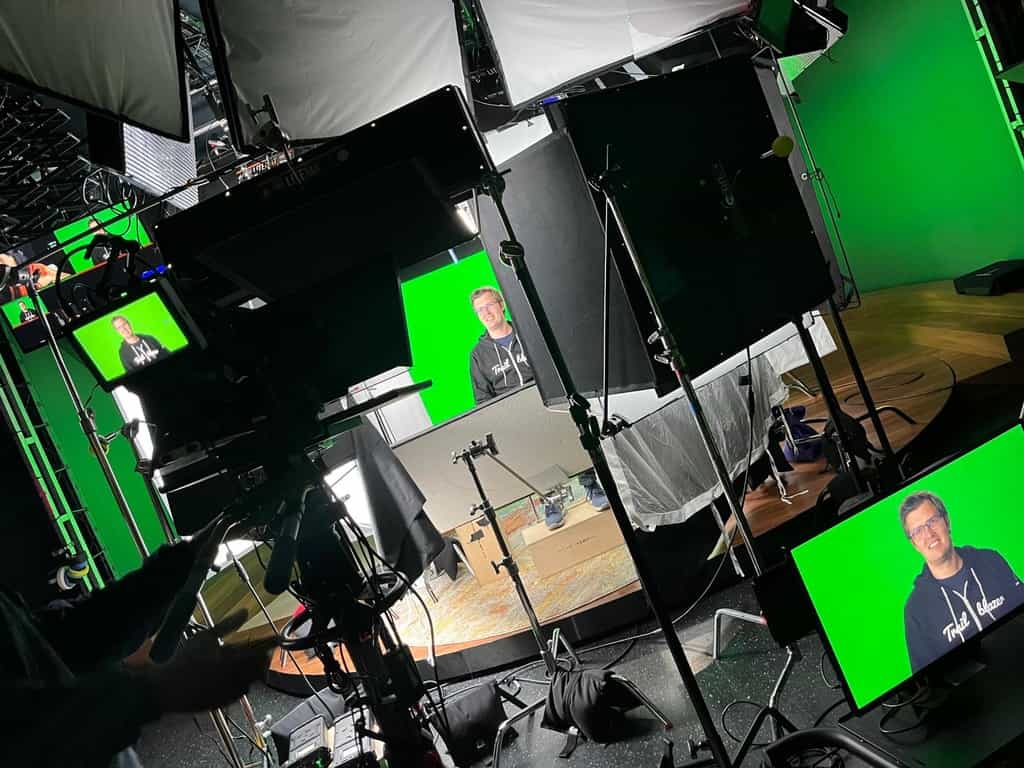 Thomas Theunen sitting in between studio lights with a camera pointed at him. Multiple screens show his face.